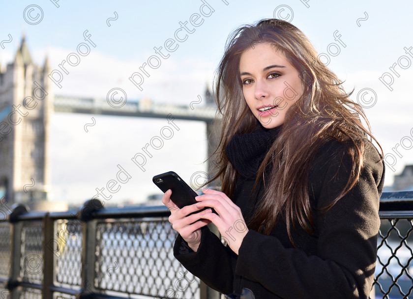 HWP1823 pp 
 Pretty long haired Brunette, in winter coat, using her mobile phone, smiling. 
 Keywords: Pretty, girl, brunette,long hair, smiling, mobile phone, texting, river background, eyes, winter coat,